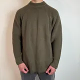 Sweater verde oliva de tejido grueso con cuello alto y mangas raglán. Corte holgado.