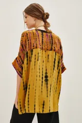 Camisa de manga corta con cuello mao y calce amplio, confeccionada en viscosa con estampado tie-dye en tonos ocre, negro y violeta. Presenta detalles bordados con mostacillas, lentejuelas, canutillos e hilos de lurex, y cierre frontal con botones a tono.