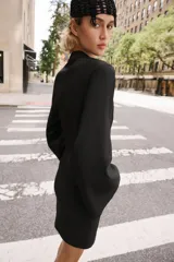 Vestido corto negro de cuello mao y escote en V, con mangas largas abanicadas y cierre de alamares en el frente. Cuenta con bolsillos frontales de plastrón y diseño de inspiración oriental.