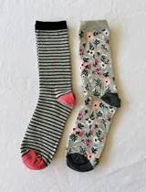 Pack de dos pares de medias de caña media. Un par a rayas horizontales en tonos gris y negro con puntera y talón rosa. El otro par en tono gris con estampado floral en blanco, rosa y negro, con puntera y talón en gris oscuro.
