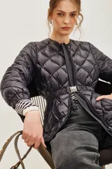 Campera acolchada de diseño matelassé con cierre frontal y cinturón ajustable con hebilla metálica. Presenta cuello redondo y mangas largas con puños elásticos.