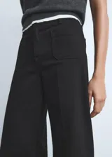 Jeans wide leg tiro alto de color negro, con cierre delantero de cremallera y botón, trabillas para cinturón y dos bolsillos de parche en la parte delantera.