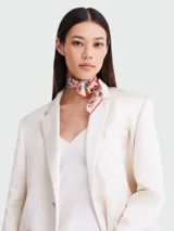 Pañuelo cuadrado de seda color rosa pálido con estampado multicolor y borde rojo.