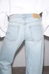 Jeans de mezclilla en color negro gastado, tiro bajo, corte de pernera recta y diseño clásico de cinco bolsillos con cierre frontal de cremallera y botón metálico.