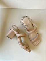 Sandalias de tacón color beige con tiras finas y hebilla en el tobillo.
