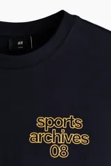 Remera boxy de algodón color negro, con cuello redondo acanalado, mangas cortas y hombros caídos. Presenta un pequeño estampado amarillo en el pecho con el texto "sports archives 08".
