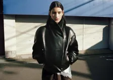 Chaqueta de estilo bomber color negro, confeccionada en 100% piel ovino con acabado de napa y diseño oversize. Cuenta con cuello alto envolvente, manga larga con puños ajustables, cierre delantero oculto con botón magnético y forro interior de poliéster.