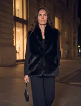 Chaleco de piel sintética negra Adrienne Landau, con cuello alto envolvente, cierre frontal oculto y bolsillos laterales funcionales. Cuenta con forro interno a tono.