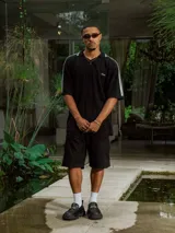 Chomba de tejido de punto cerrado, color blanco, con cuello polo y tapeta de botones. Presenta franjas deportivas blancas en los hombros y mangas cortas. Lleva un bordado pequeño en el pecho.