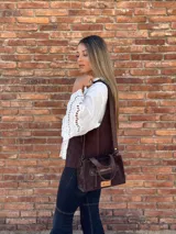 Cartera bandolera de cuero color marrón chocolate, con forro de tela y herrajes dorados. Tiene doble asa de mano y correa larga regulable y desmontable. Incluye bolsillo frontal con cierre y bolsillo interno.