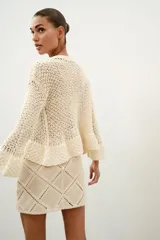 Minifalda de tiro medio confeccionada en ante color beige, decorada con aplicaciones de tejido tipo crochet blanco formando un patrón de rombos. Cuenta con cierre de cremallera oculta en la costura.