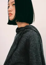 Jersey de punto fino color gris, con cuello redondo y una bufanda integrada del mismo género que cuelga al frente. Cuenta con diseño de manga larga y corte recto.