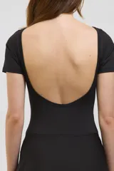Vestido deportivo corto de color negro, diseñado para pádel. Presenta una estructura superior tipo remera de manga corta con espalda abierta, y una parte inferior que combina una calza corta con una media pollera envolvente que se ata en la cintura. Confeccionado en tejido suave y elástico.