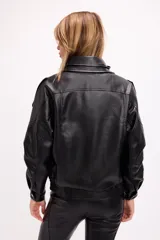 Campera estilo bomber oversize confeccionada en símil cuero negro con textura granulada. Presenta cuello alto con cierre frontal, hombreras marcadas, bolsillos laterales y cintura con elástico y cinto ajustable con hebilla metálica.