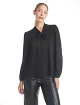 Blusa de seda fría color negro, con escote en V y lazo decorativo al cuello. Presenta mangas largas abullonadas con puños elásticos y detalles de strass aplicados en cuello, lazo y mangas.