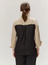 Camisa de lino color blanco con detalles combinados en tonos beige, cuello camisero, cierre frontal con botones oscuros y mangas largas con puños en contraste.
