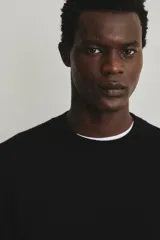 Buzo de punto fino color negro, con cuello redondo y remates acanalados en cuello, puños y bajo. Corte estándar.