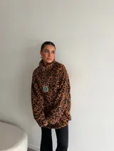 Buzo de peluche con estampado animal print, cuello alto con cierre frontal parcial y detalle de etiqueta decorativa en el pecho.