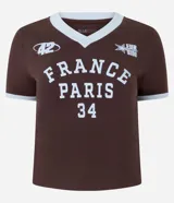 Remera femenina de media malla de algodón color marrón, con cuello en V y ribetes celestes en cuello y mangas. Presenta un estampado frontal con el lettering "France Paris 34" en celeste, junto con detalles deportivos como un logo "42" y una estrella con "Leurside".