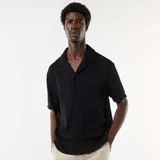 Camisa de punto calado negro, de manga corta, con cuello solapa y cierre frontal de botones.