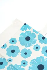 Bolso tipo tote bag de color crudo con estampado de flores celestes y centros azul oscuro. Cuenta con doble asa de hombro en tono crudo y etiqueta con la marca en el frente.