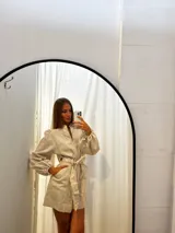 Mono corto de lino color beige, con cuello camisero, cierre frontal, mangas largas abullonadas y cinto ajustable en la cintura.