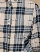 Camisa de manga larga con estampado de rayas verticales en tonos blanco y lila. Presenta cuello alto con volados, cierre frontal con doble botonadura y puños con volados.