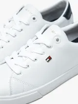 Zapatillas urbanas Tommy Hilfiger de corte bajo, color blanco con detalle azul en el talón. Tienen diseño con cordones, suela de goma blanca y pequeño logo bordado en el lateral.