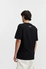 Remera de manga corta color beige, con escote redondo y fit regular. Presenta un estampado frontal en color marrón con la palabra "Resilience" en tipografía gótica y el texto "Original The World Has Changed Established Since 1976 // NLD Mistral".