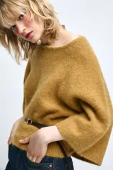 Jersey de punto color mostaza con cuello redondo y mangas amplias tipo murciélago. Presenta un diseño ajustado en la cintura con un cinturón fino de cuero sintético en color marrón a contraste.