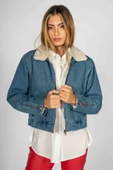 Campera de jean azul con cuello de piel sintética color crema, cierre frontal y cierres decorativos en los puños.