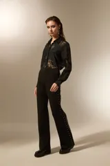 Pantalón tipo calza flare de tiro alto, color negro, con detalle de tachas metálicas plateadas a lo largo de las costuras laterales.