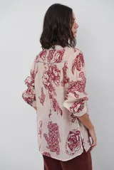 Camisa de corte holgado con estampado floral en tonos rojizos sobre base clara. Presenta cuello mao con escote en V y cierre frontal parcial con botones, además de mangas largas con puños ajustados.