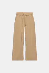 Pantalón recto color beige de tiro medio, con cintura elástica, bolsillos delanteros y cinturón ajustable con hebilla metálica dorada.