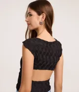 Blusa sin mangas de color negro, confeccionada en tejido texturizado con cuello redondo y abertura en la espalda.