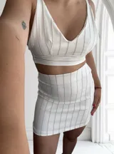 Conjunto de top y pollera a rayas verticales color blanco y beige. El top es corto, con breteles finos y escote en V. La pollera es corta y ajustada al cuerpo.