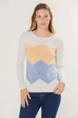 Buzo de tejido de punto fino con diseño de bloques de color en forma de zigzag en tonos lila y amarillo sobre base color crema. Presenta cuello redondo y mangas largas.