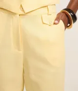 Pantalón carrot de cintura alta, confeccionado en mezcla de viscosa y lino, con trabillas en la cintura, pliegues y solapas con botón decorativo. Presenta un corte holgado en las caderas que se estrecha hacia los tobillos.