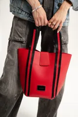 Bolso tipo tote de color rojo con textura símil cuero, cierre con imán, doble asa de mano con detalles de rayas negras y etiqueta metálica con el logo de la marca. Incluye necessaire con cierre.