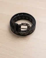 Cinto de dama de símil cuero negro, con ojales metálicos y una hebilla grande con diseño ornamental de estilo western.