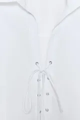 Camisa entallada de popelín con cuello solapa y escote en pico. Presenta manga larga con puños y un diseño frontal con cordones cruzados y lazada. Incluye cierre lateral con cremallera oculta.