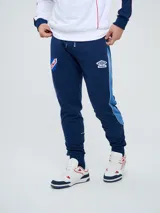 Pantalón de jogging azul marino Umbro del Club Nacional de Football, con cordón ajustable en la cintura, puños elastizados en los tobillos y bandas laterales en tonos de azul. Cuenta con el escudo del club en una pierna y el logo de la marca en la otra.