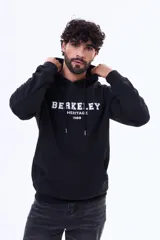 Buzo tipo canguro de felpa color negro, con capucha ajustable mediante cordones, bolsillo frontal tipo canguro y estampa frontal con texto universitario.