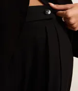 Pantalón de vestir negro, corte pantalona ancho y fluido, con pliegues frontales y cierre de botón en la cintura.