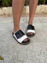 Sandalias bajas con base color suela, tira ancha delantera de cuero sintético blanco con textura reptil y tira superior de cuero sintético negro con textura reptil.