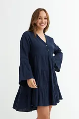 Vestido corto color verde oliva, con escote en V y botones frontales. Presenta mangas 3/4 con volados y falda con diseño de volados escalonados.