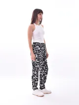 Pantalón babucha de tiro alto con cintura fruncida y lazo para ajustar. Estampado de hojas tropicales en tonos naranja y marrón sobre fondo blanco.