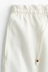 Short de denim liviano color blanco, confeccionado en mezcla de algodón y lyocell. Presenta tiro alto con cintura elástica de volado, cordón de ajuste fino con terminales de metal y bolsillos laterales discretos.