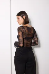 Remera de encaje negro con diseño asimétrico, manga larga y cuello redondo. Presenta un patrón floral y un corte ajustado al cuerpo.