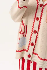 Saco oversize tejido con ilustraciones inspiradas en corales, peces, estrellas de mar y tortugas. Presenta galón picot en rojo en cartera y puños, y botones a tono.